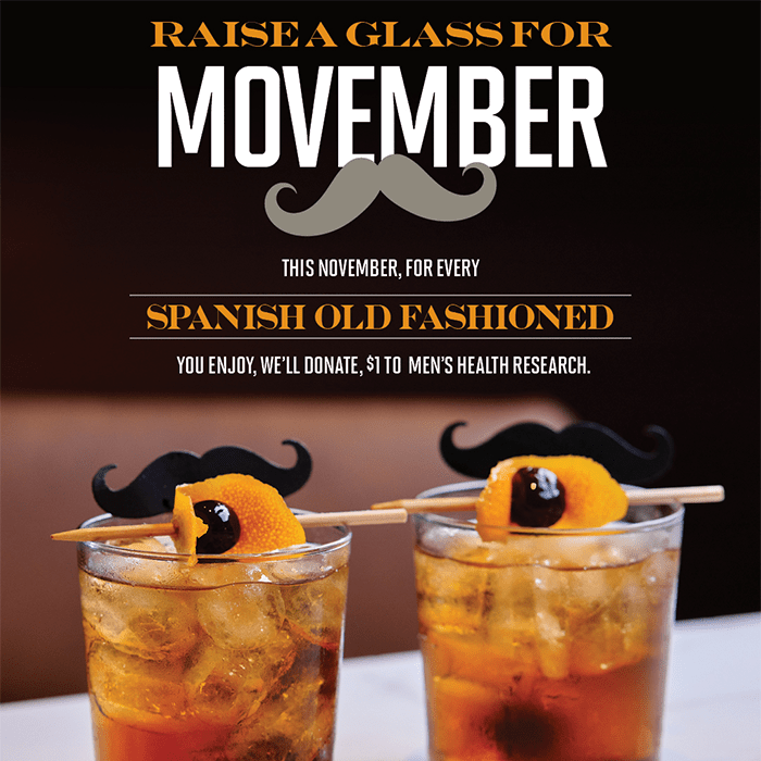 Two Spanish Old Fashioned cocktails garnished with orange peel, cherry, and mustache stick for Movember promotion.