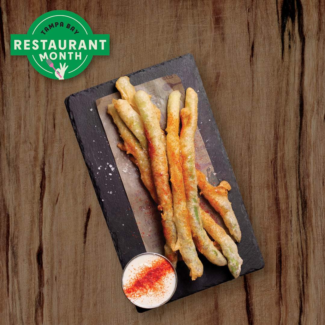 Bulla Gastrobar Tampa Bay Restaurant Month promotional graphic featuring Spanish dishes on a wood table, including tapas, paella, salmon, and churros, with Bulla Gastrobar,