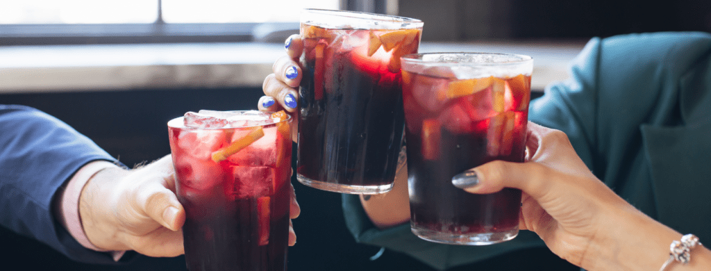 Glasses of red sangría with fresh fruit served on a wooden table.