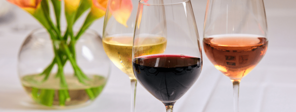 Glasses of red, white, and rosé wine on a table with a floral arrangement in the background